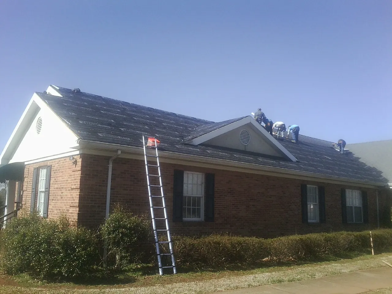 Crew tearing shingles off a brick ranch roof with a ladder set — Metal Roof Repair work by our crew in Cammal