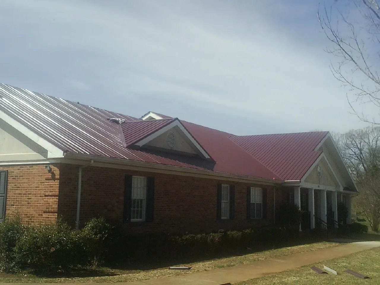 Red metal roof with gabled entries on a long brick building, from a Hail Damage Roof Repair job in Cammal