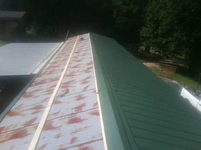 Old rusted panels beside newly installed green metal roofing — Wind Damage Roof Repair by Roofing Brothers in Cammal
