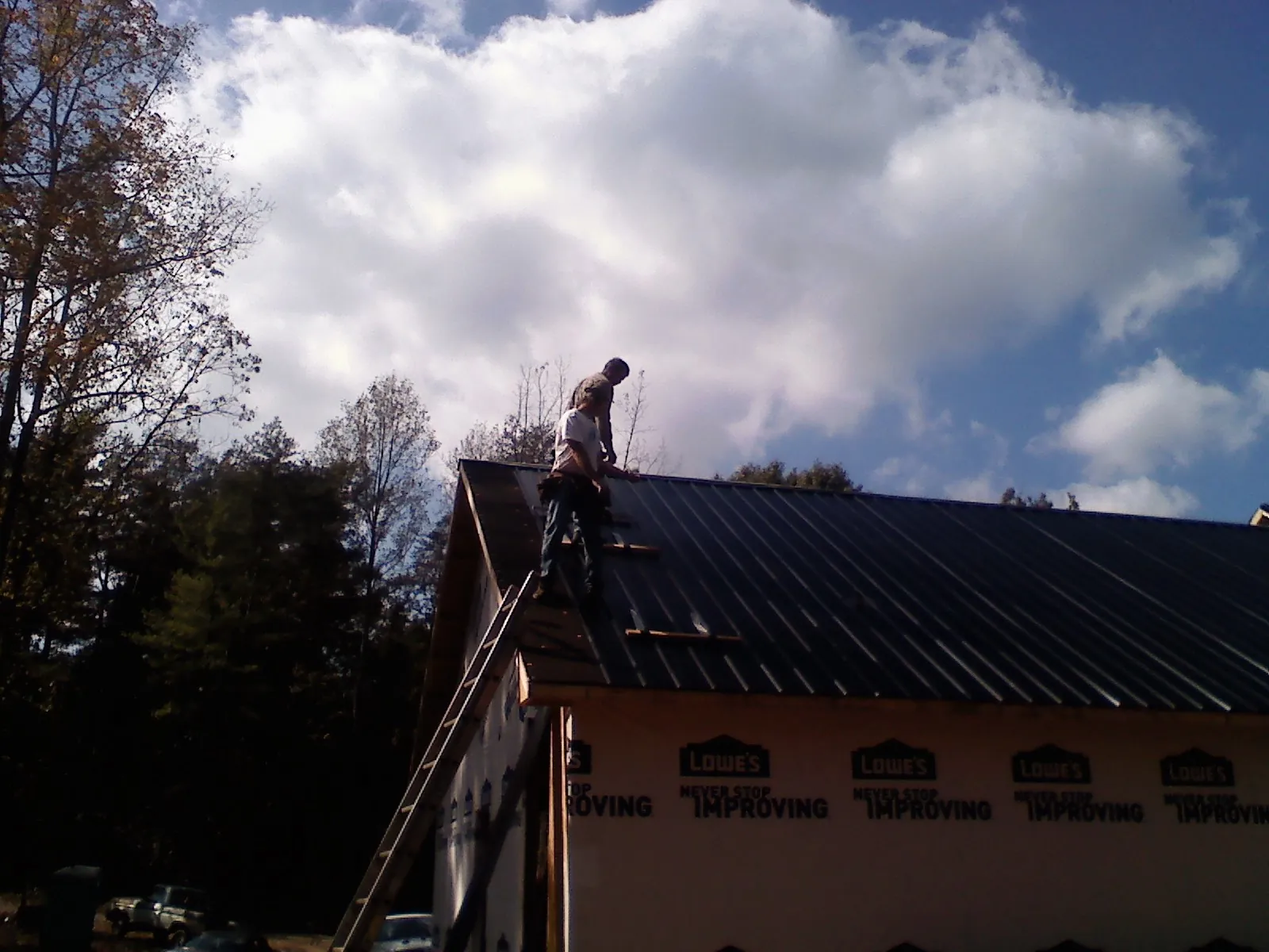Roofer fastening dark metal panels high against a cloudy sky, from a Roof Inspection job in Cammal