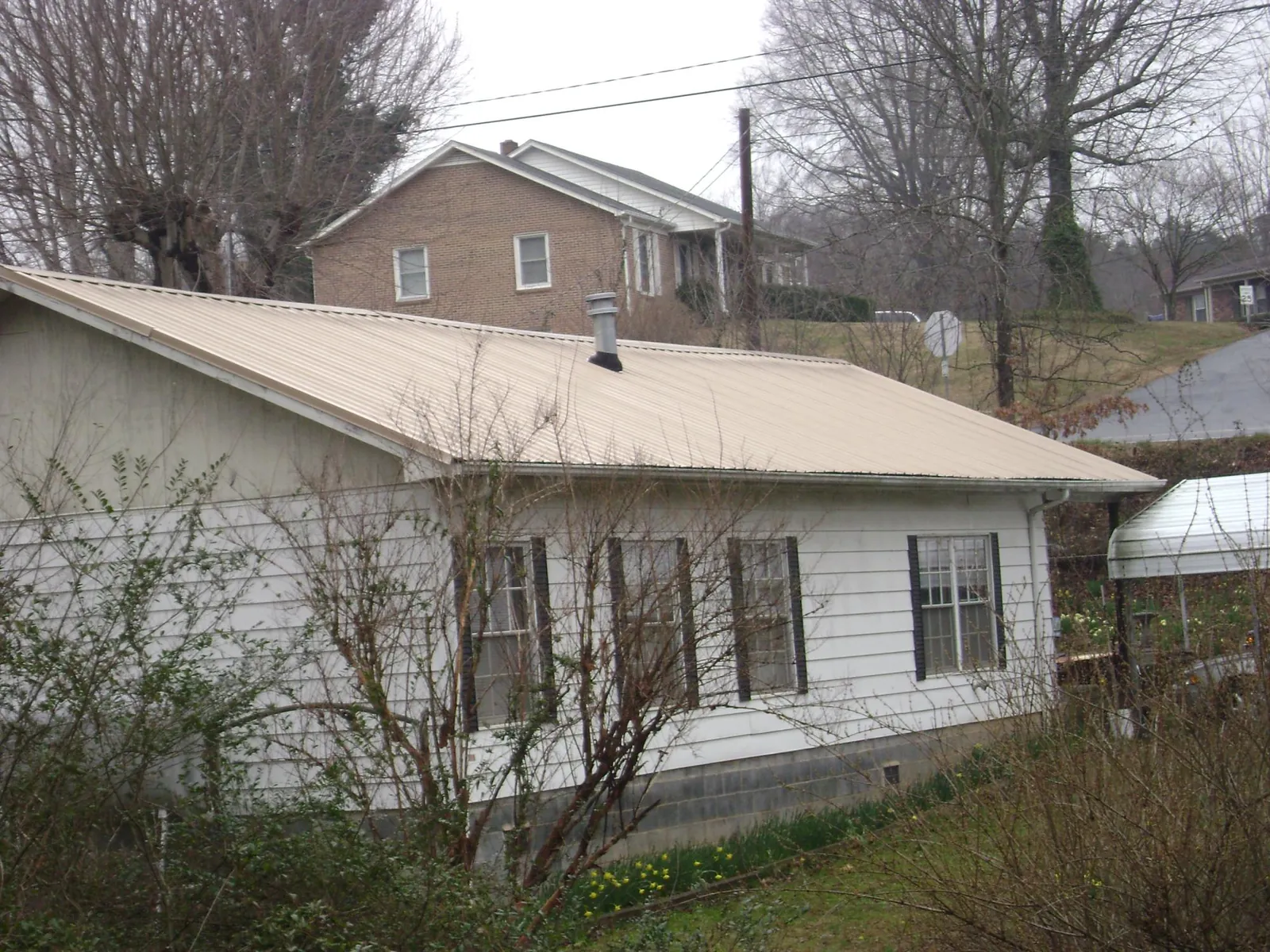Tan metal roof on a white sided house set into a hillside — Commercial Roofing by Roofing Brothers in Cammal